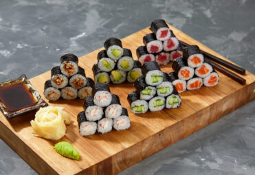 Assortment of different kinds of sushi rolls placed on black stone board. Sushi set with salmon, cucumbers, cream cheese, avocado and sesame seeds. Sushi image for menu.