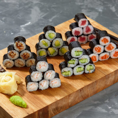 Assortment of different kinds of sushi rolls placed on black stone board. Sushi set with salmon, cucumbers, cream cheese, avocado and sesame seeds. Sushi image for menu.
